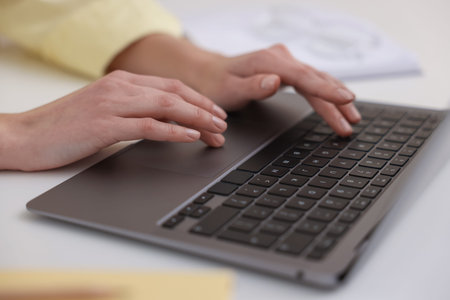 Woman working on laptop at white table, closeup