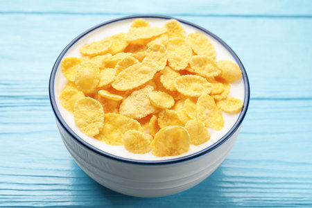 Tasty corn flakes with milk in bowl on light blue wooden table, closeup