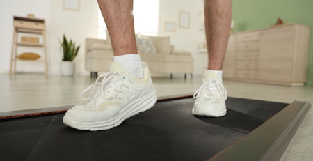 Sporty man training on treadmill at home, closeup