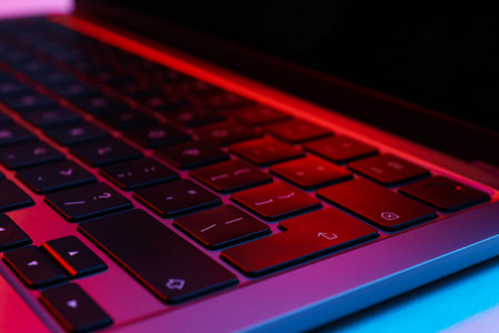 Stylish modern laptop in neon lights on white background, closeup