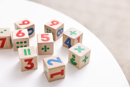 Wooden cubes with numbers and symbols on white table indoors, closeup