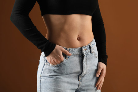 Woman with belly button piercing on brown background, closeup