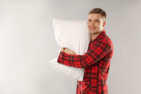 Man in stylish pyjamas with pillow on light grey background, space for text