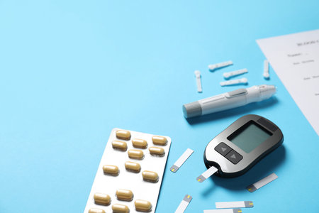 Diabetes. Digital glucometer, test strips, pills and lancet pen on light blue background, closeup....