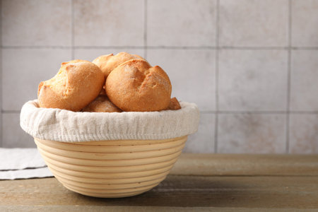Delicious freshly baked buns in bowl on wooden table indoors, closeup. Space for text