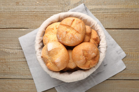 Delicious freshly baked buns in bowl on wooden table, top view