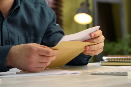 Man opening envelope with letter at white wooden table indoors, closeup
