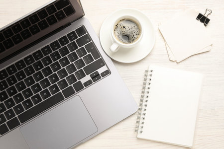 Laptop, stationery and coffee on light wooden table, flat lay
