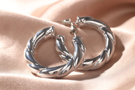 Shiny silver earrings on pink silk cloth, closeup