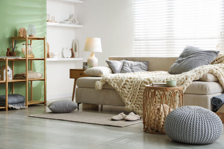 Beautiful sofa with knitted plaid and pillows in living room. Interior design