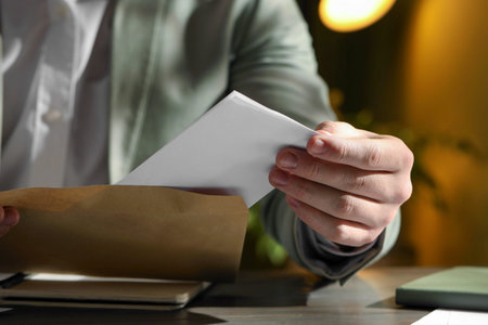 Man putting letter into envelope at wooden table indoors, closeup