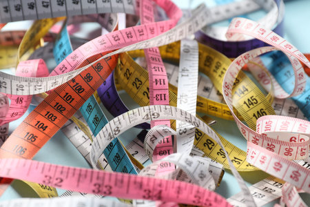 Different measuring tapes on light blue background, closeup