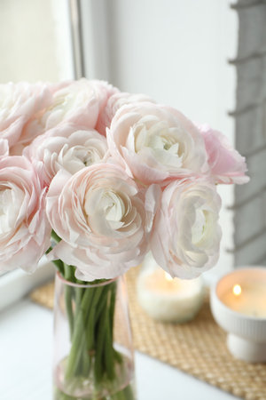 Beautiful ranunculus flowers in glass vase on white window sill indoors, closeup