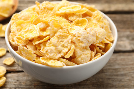Tasty corn flakes in bowl on wooden table, closeup