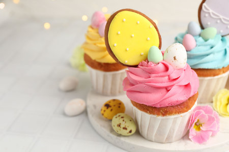 Tasty cupcakes with Easter decor on white tiled table, closeup. Space for text