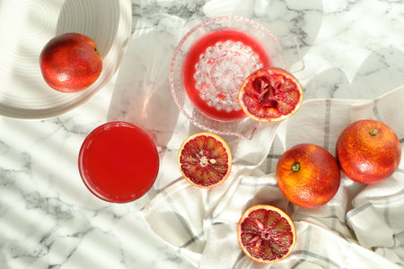 Ripe Sicilian oranges, glass of juice and squeezer on white marble table, flat lay