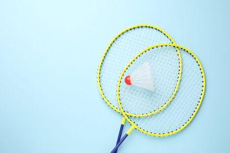 Badminton shuttlecock and rackets on light blue background, flat lay. Space for text