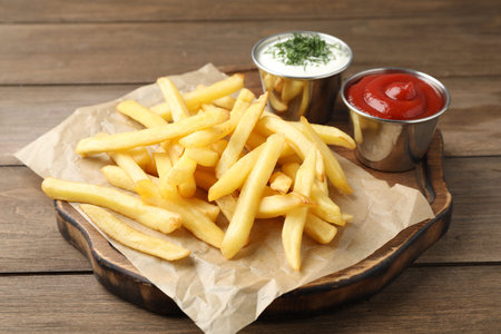 Tasty french fries with sauces on wooden table, closeup