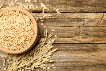 Oat flakes in bowl and panicles on wooden table, flat lay. Space for text