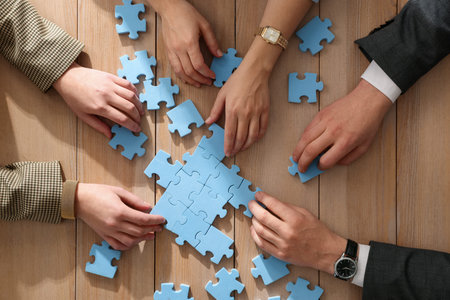 Team building. Group of businesspeople solving puzzle together at wooden table, top view