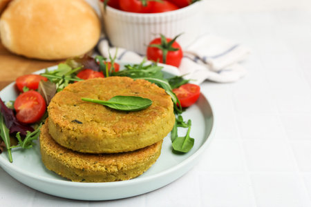 Tasty vegan patties with salad served on white tiled table, closeup