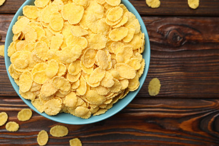 Tasty corn flakes in bowl on wooden table, top view. Space for text