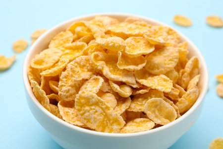 Tasty corn flakes in bowl on light blue background, closeup