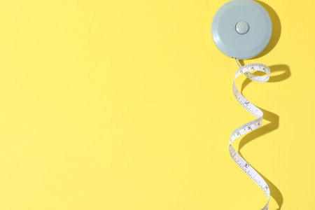 One measuring tape on yellow background, top view. Space for text