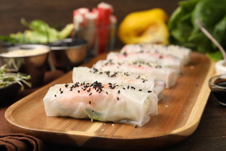 Fresh spring rolls with rice paper and sesame seeds on wooden table, closeup