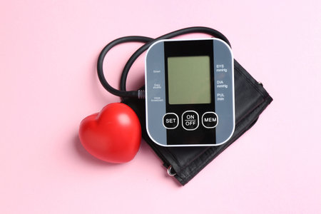 Measuring blood pressure. Sphygmomanometer and red heart figure on pink background, top view