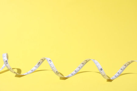 One measuring tape on yellow background, top view. Space for text