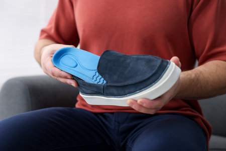 Man putting orthopedic insole into shoe indoors, closeupの写真素材