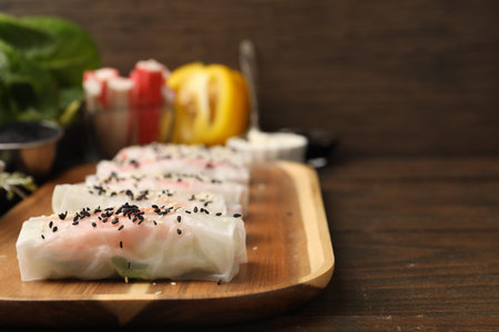 Fresh spring rolls with rice paper and sesame seeds on wooden table, closeup. Space for text