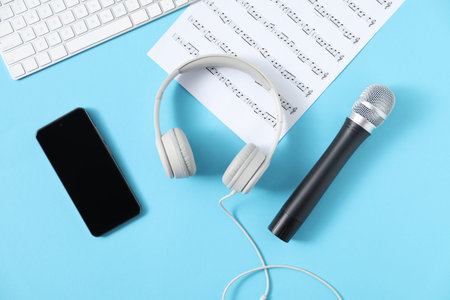 Headphones, microphone, computer keyboard, music sheet and smartphone on light blue background, flat...