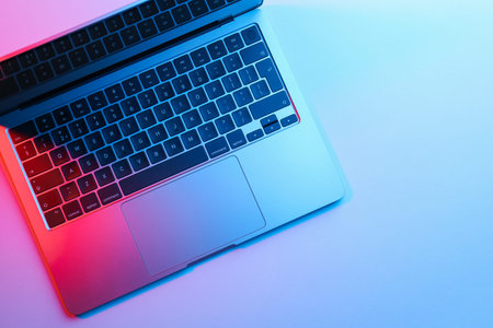 Modern laptop in neon lights on light table, top view. Space for text