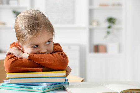 Fatigue. Little girl with stack of books at white table indoors, space for text