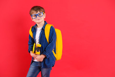 School holidays. Cute boy with backpack and penny board on red background, space for text