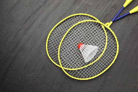 Badminton rackets and shuttlecock on black table, top view. Space for text