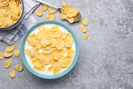 Tasty corn flakes with milk in bowl served on grey table, flat lay. Space for text