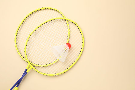 Badminton rackets and shuttlecock on beige background, top view. Space for text
