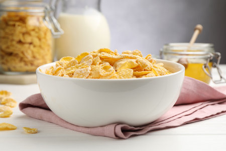 Tasty corn flakes in bowl served on white wooden table, closeup