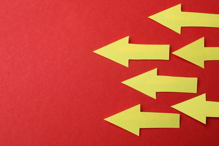 Yellow paper arrows on red background, flat lay. Space for text