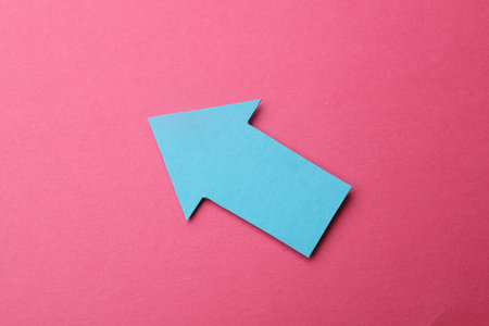 Light blue paper arrow on pink background, top view