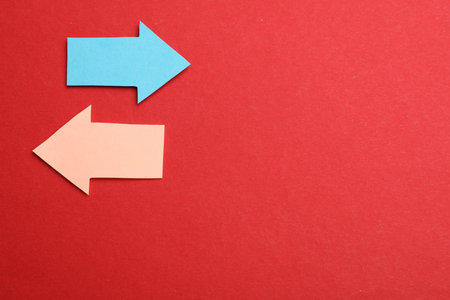 Colorful paper arrows on red background, flat lay. Space for text