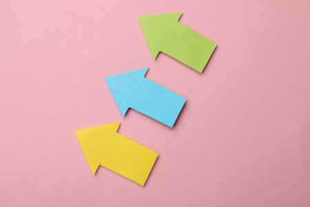 Colorful paper arrows on pink background, flat lay