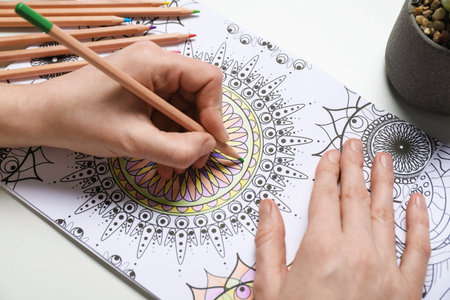 Woman coloring antistress picture with pencils at white table, closeupの写真素材