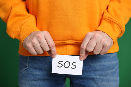 Urology. Man holding note with word SOS on green background, closeup