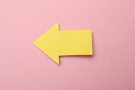 Yellow paper arrow on pink background, top view