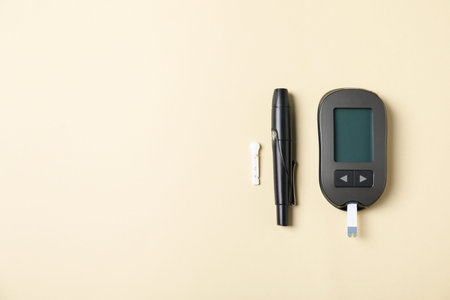 Diabetes. Digital glucometer with test strip, pen and lancet on beige background, flat lay. Space...