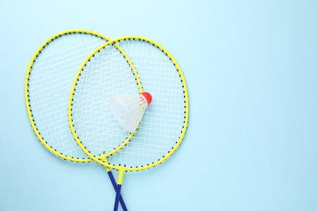 Badminton shuttlecock and rackets on light blue background, flat lay. Space for text